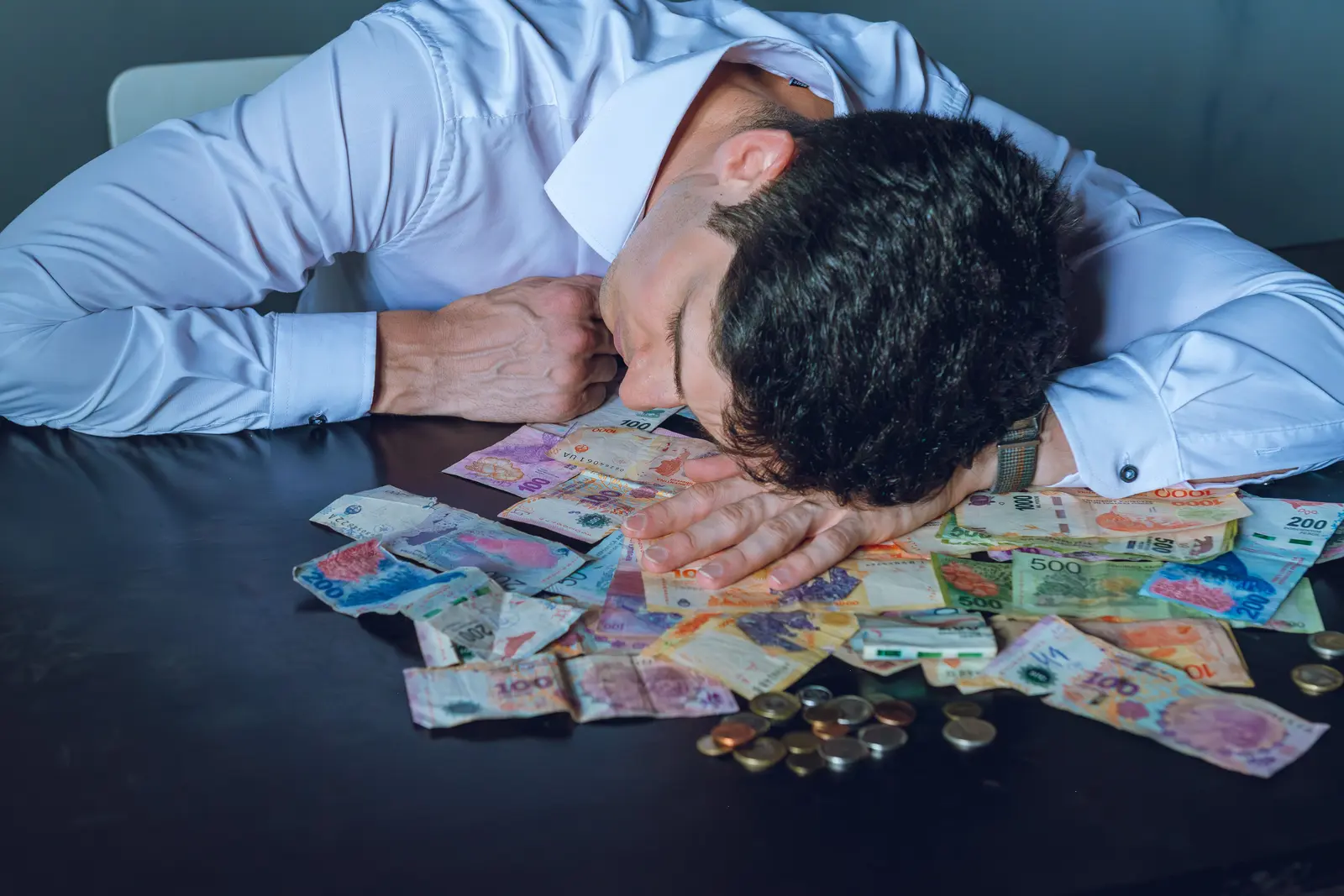 A man slumped over a desk scattered with banknotes and coins