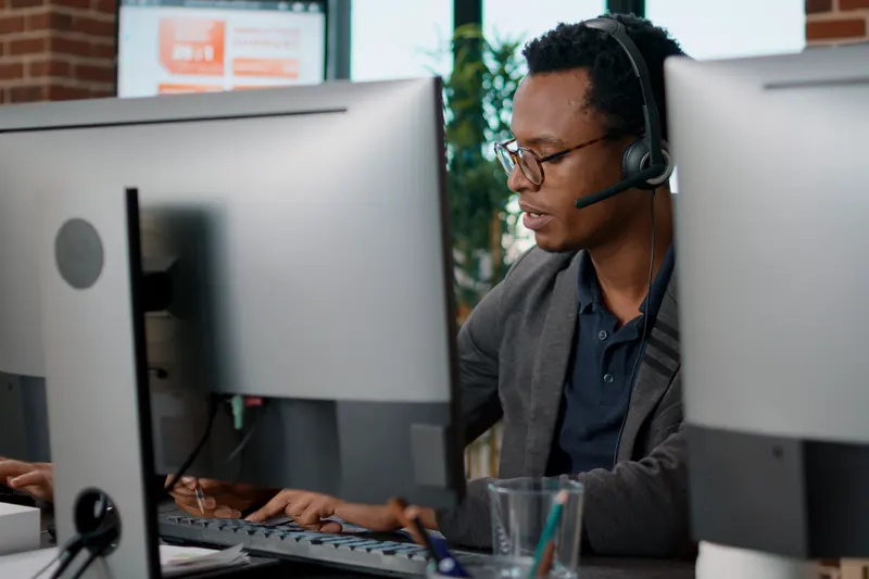 A call-centre agent wearing a headset at a bank of monitors